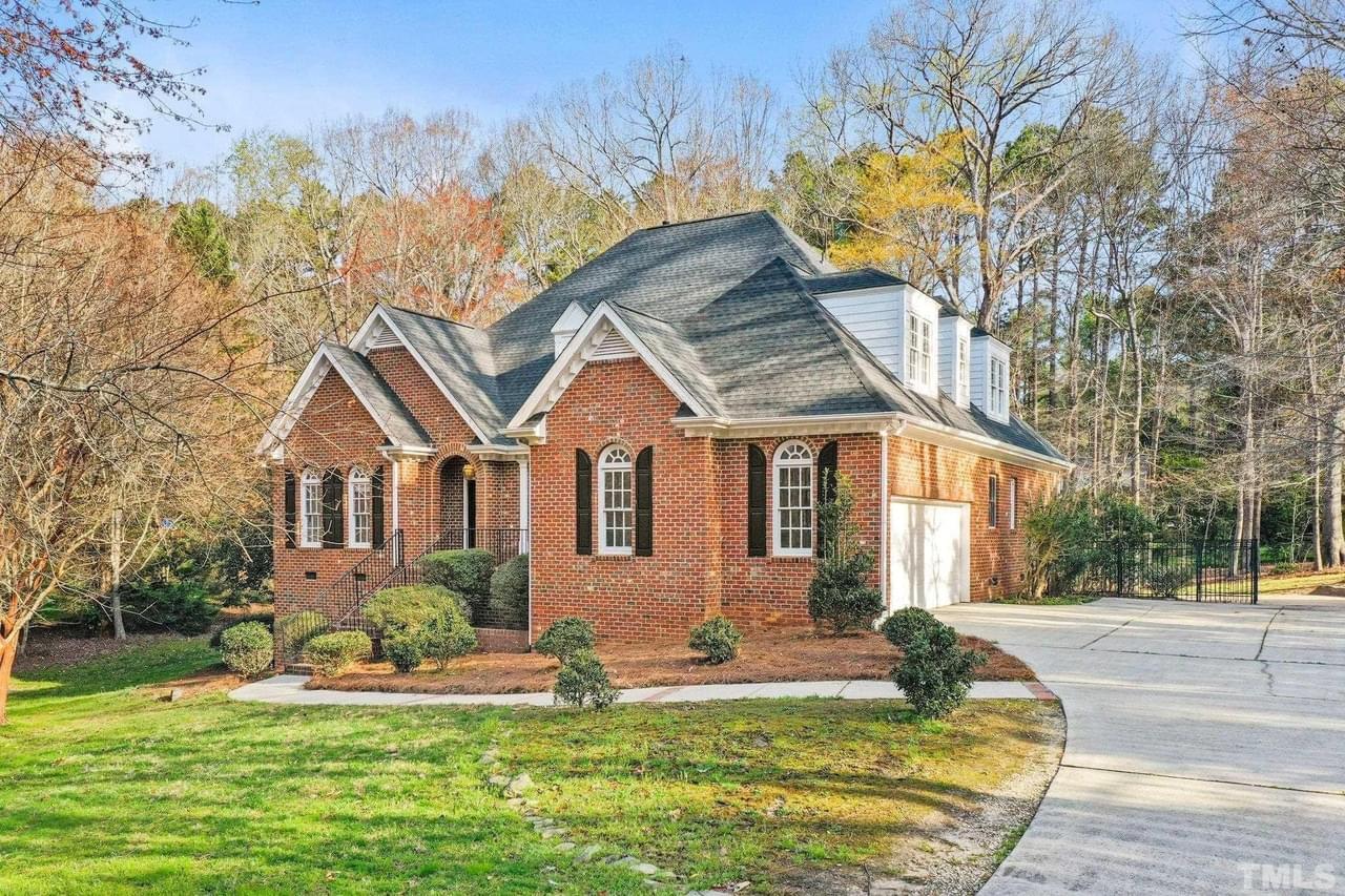 A classic brick home with a large lot, many trees, arched windows with shutters, and a green lawn